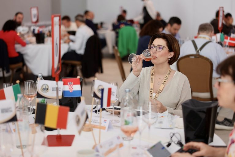 Degustătoare de vin rosé în cadrul Concours Mondial de Bruxelles, la o masă cu stegulețe internaționale.