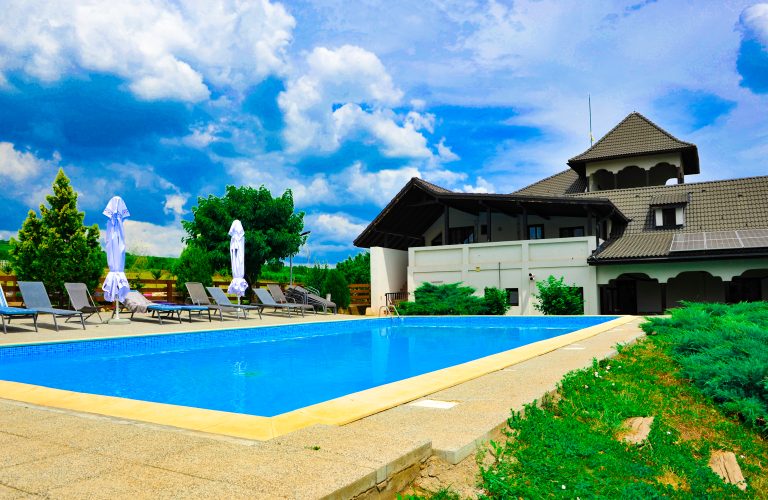 Piscină modernă la o cramă din Dealu Mare, înconjurată de verdeață și clădire tradițională