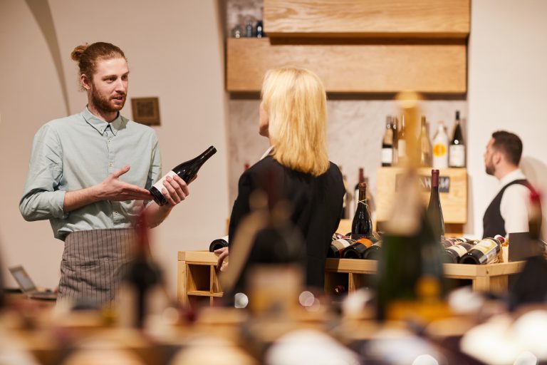 Consultant de vin prezentând o sticlă unui client