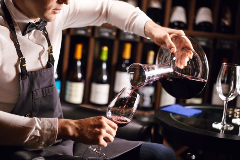 Somelier turnând vin roșu din decantor în pahar