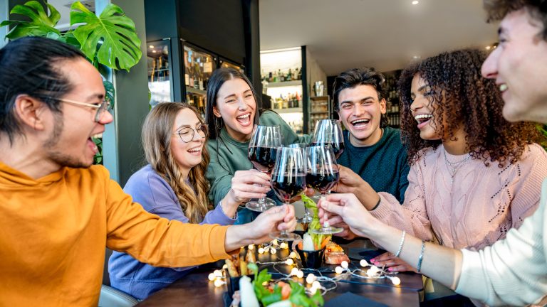 Grup de prieteni tineri, multietnic, ciocnind pahare de vin roșu într-un restaurant modern