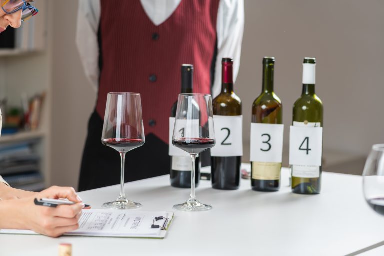 Degustare de vinuri în orb, cu sticle numerotate și note de evaluare pe masă.