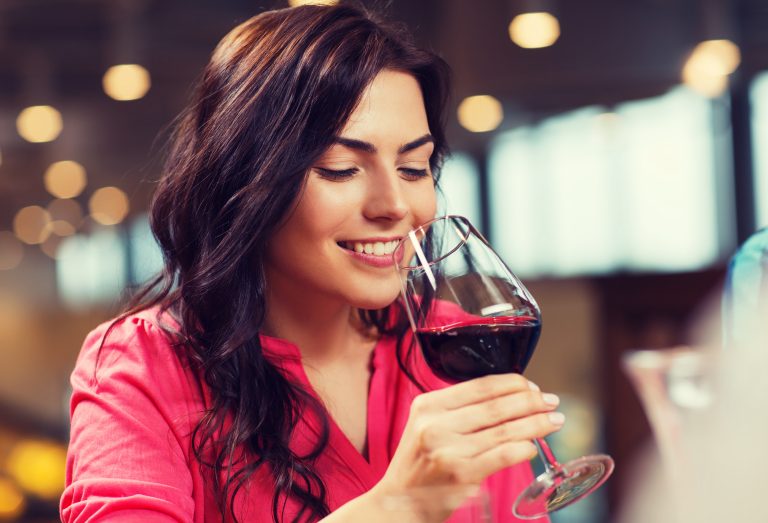 Femeie tânără zâmbitoare savurând aroma unui vin bun