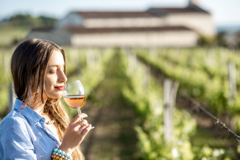 Femeie degustând un pahar de vin rosé într-o podgorie, bucurându-se de aromele vinului românesc.